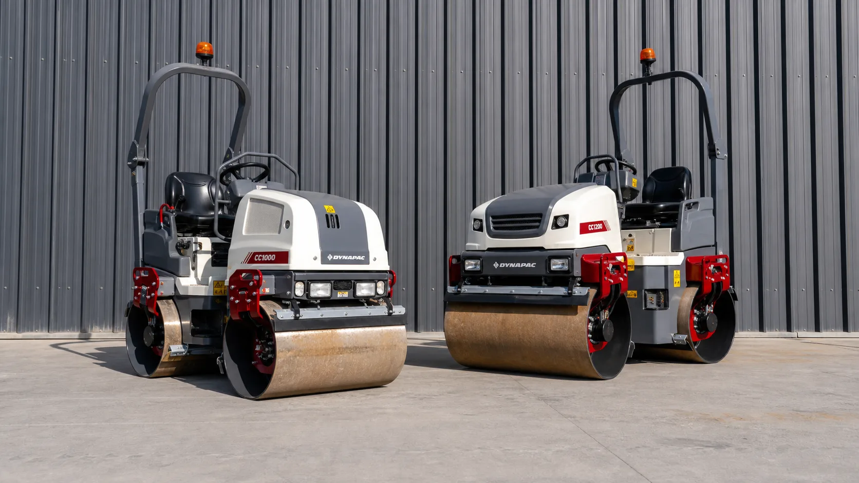 Dynapac CC1000 and CC1200 tandem asphalt rollers parked in front of a metal building